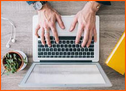 Hands on a keyboard with earbuds, a plant, and a book nearby