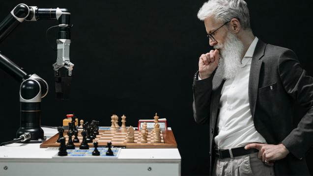 Man playing chess with an opponent that is a robotic arm.