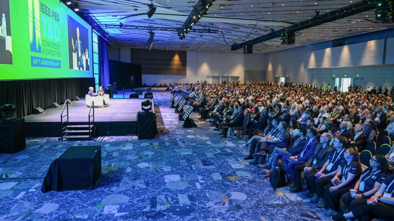 A conference event with several panelists sitting on a stage and a full audience.