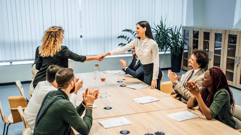 Two women shaking hands from across a conference room table.