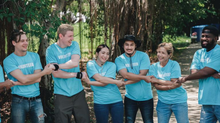 Several people smiling and linking arms. They are wearing light blue t-shirts with the word "Volunteer" on them