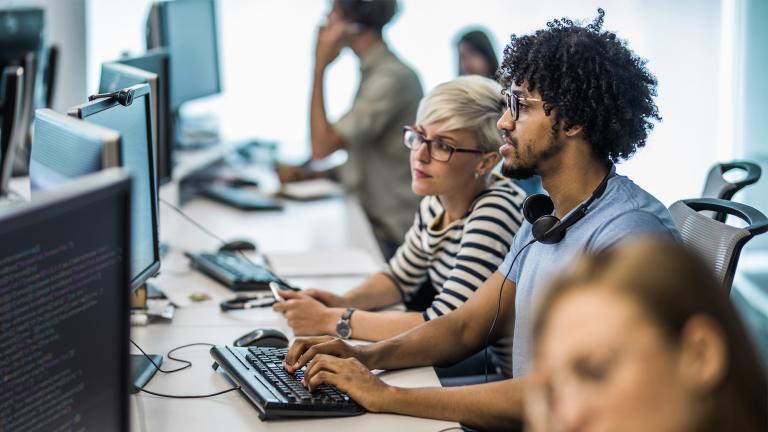 Three people huddling around of a computer