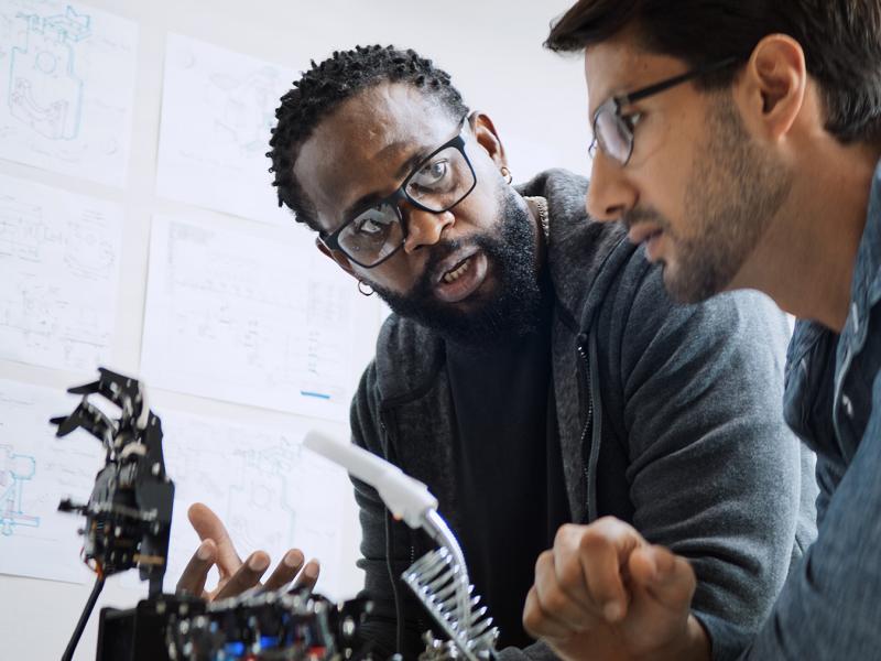 Two men working on a piece of tech, talking animatedly