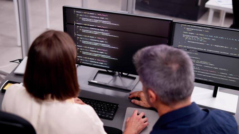 Two individuals sitting in front of two monitors working on code