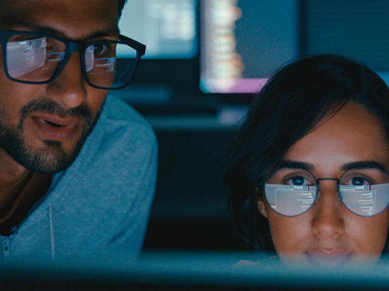 Two young adults wearing glasses looking at a computer